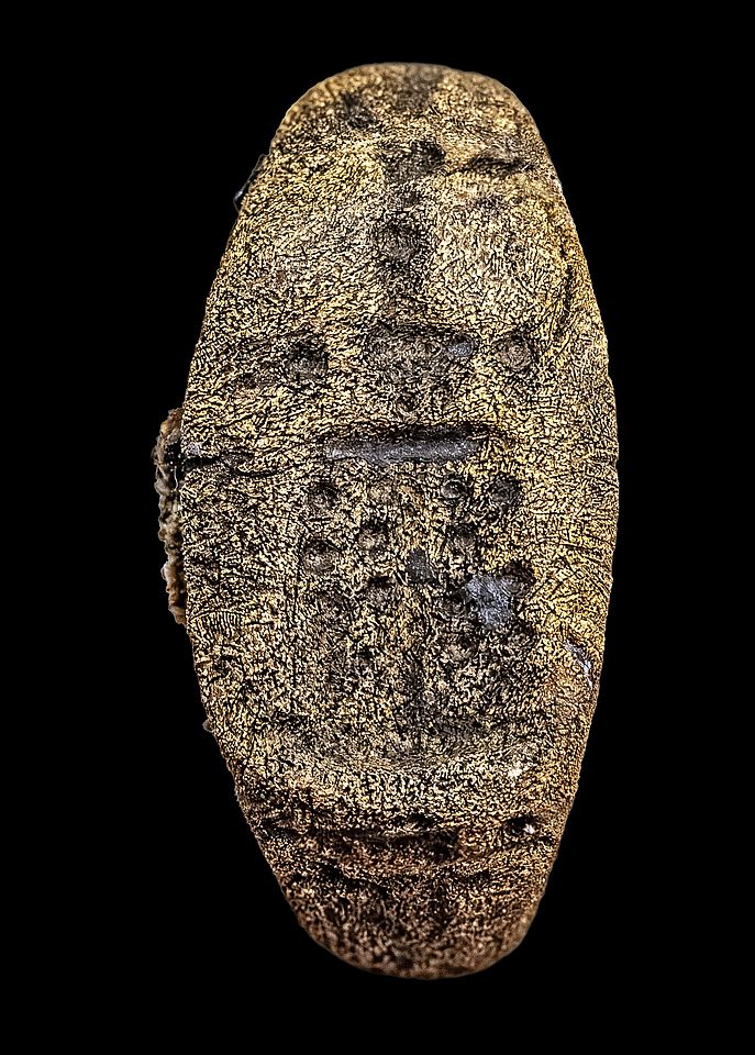 Close-up of an ancient bronze signet ring against a black background, featuring a weathered engraving of the Lighthouse of Alexandria.